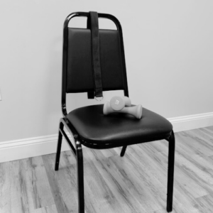 Chair against a blank wall with a strap over the top and a set of light dumbbells on the seat.
